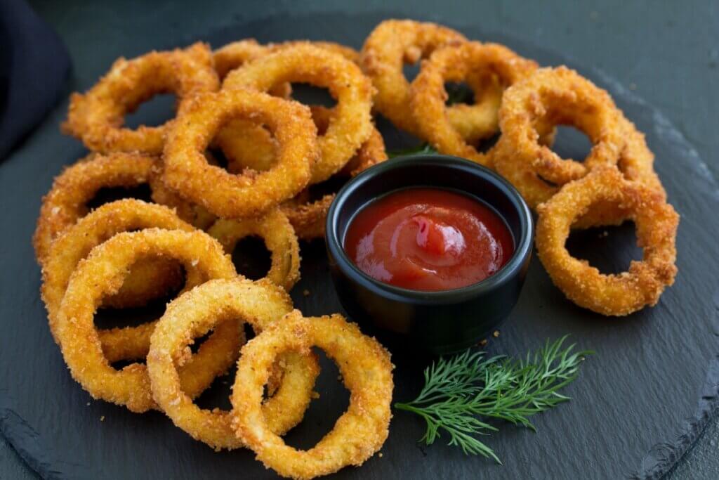 Onion rings servida em bancada de cerâmica com pote com ketchup ao lado