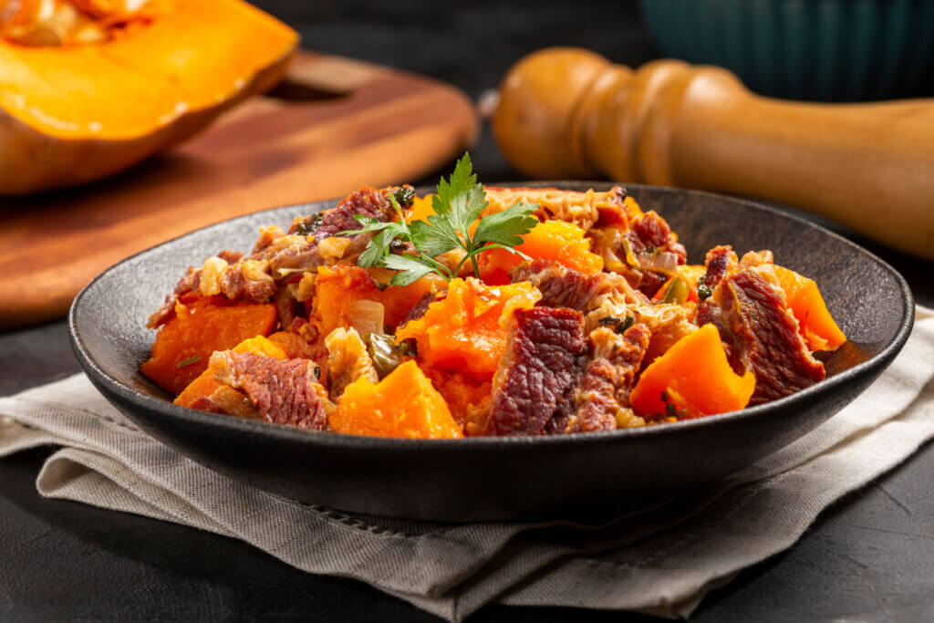 Carne-seca com abóbora em um prato preto decorado com coentro