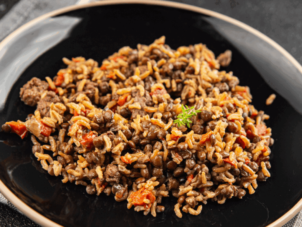 Prato de arroz com lentilhas, pimentão vermelho e temperos servido em prato preto