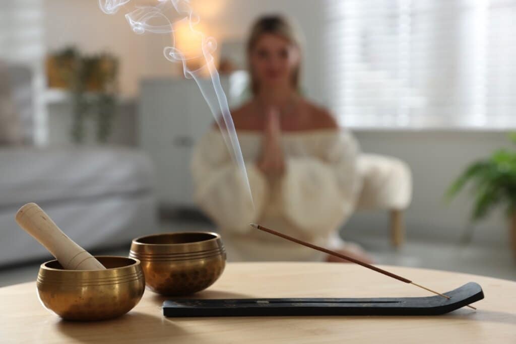 Incenso aceso em cima de uma mesa com uma mulher sentada meditando ao fundo