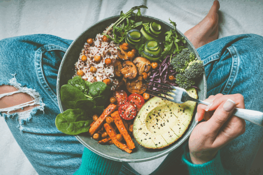 Mãos feminina segurando bowl com brócolis, cenoura, abacate, arroz, cogumelo e grão-de-bico