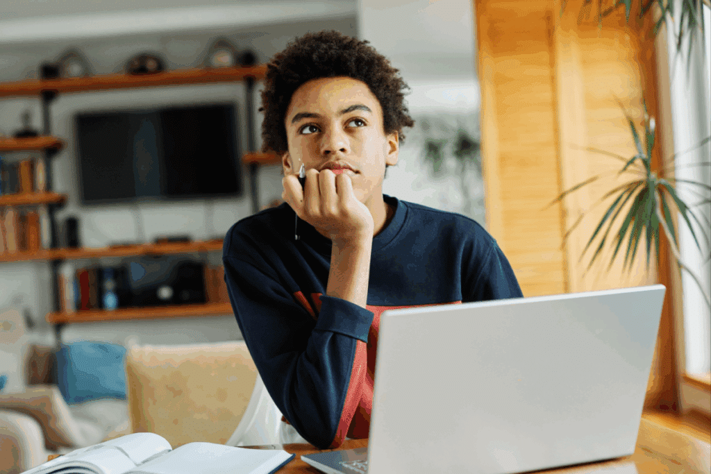 Jovem sentado em frente a um notebook e pensativo