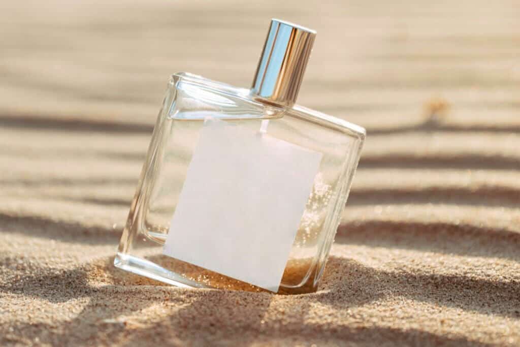 Frasco de perfume com rótulo branco na areia