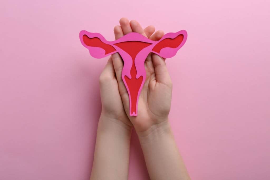 Imagem de duas mãos segurando o desenho de um útero em um fundo rosa