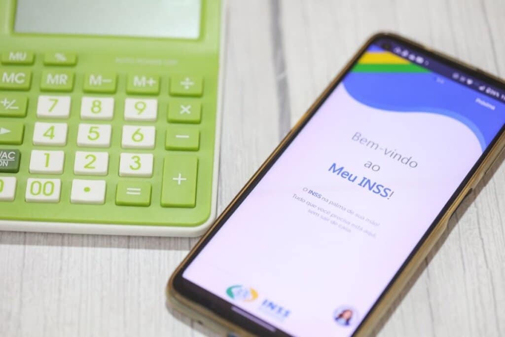 Celular com a tela aberta no aplicativo Meu INSS ao lado de uma calculadora verde sobre uma mesa