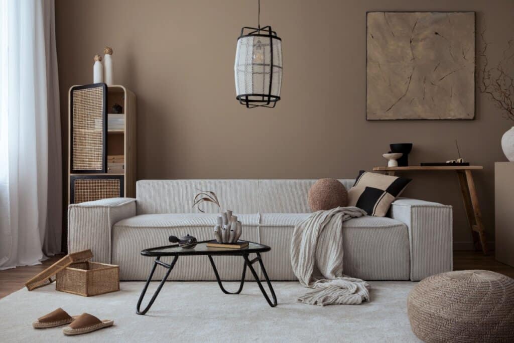 Sala de estar aconchegante em tons terrosos, com sofá claro, luminária pendente, mesa de centro preta e elementos decorativos naturais