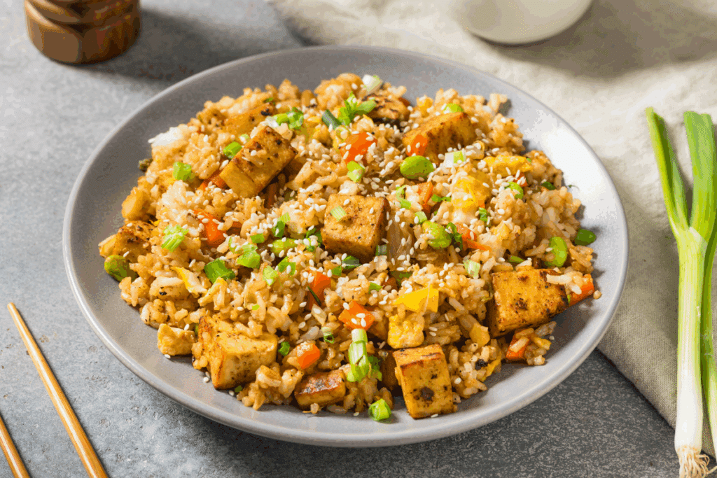 Arroz com tofu, legumes e ovos servido em prato fundo cinza em cima de bancada cinza