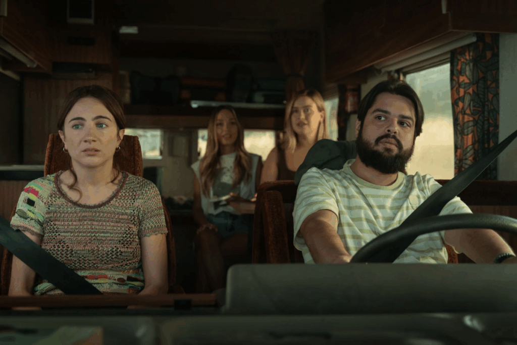 Quatro pessoas dentro de um trailer em movimento; um homem com barba dirige e uma mulher no banco do passageiro olha para a frente com expressão apreensiva.