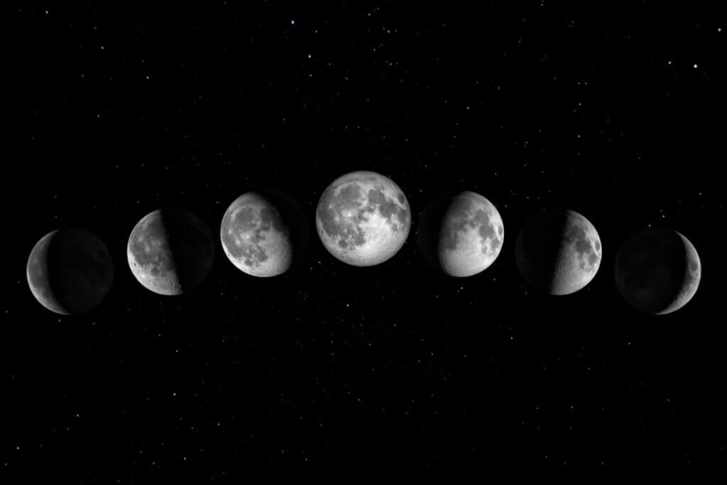 Uma montagem fotográfica mostrando sete fases da lua dispostas em um arco horizontal sobre um fundo de céu noturno preto e estrelado. A sequência começa à esquerda com uma lua crescente tênue, progride para a lua cheia brilhante no centro do arco e termina à direita com uma lua minguante fina. As crateras e detalhes da superfície lunar são visíveis em tons de cinza e branco contra o contraste escuro do espaço.