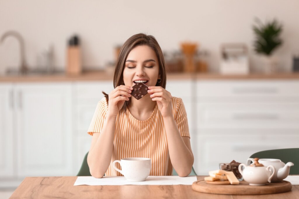 Mulher sentada e comendo chocolate em uma cozinha