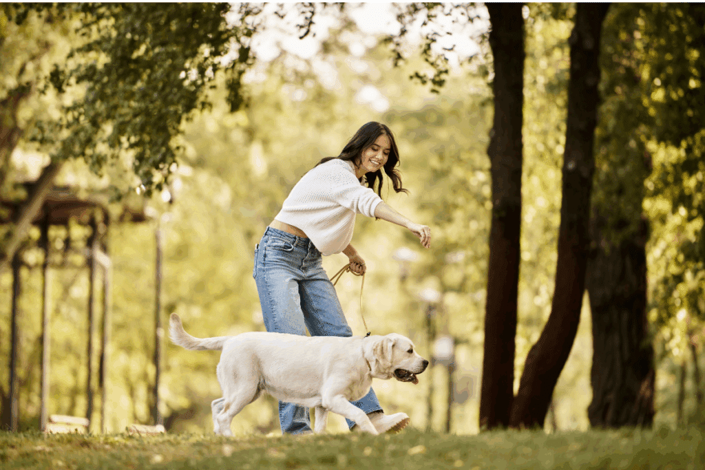 Mulher brincando com um cachorro, com pelagem bege-claro, em parque