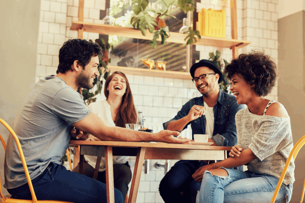 Grupo de amigos conversando e dando risada sentados em mesa de lanchonete