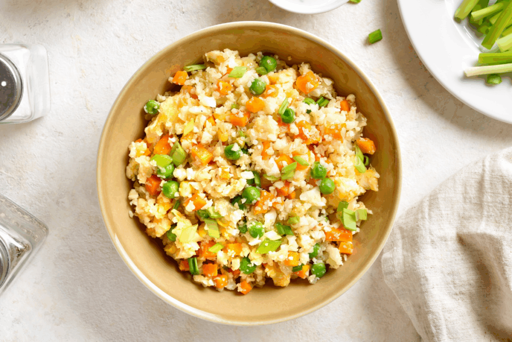 Arroz de couve-flor com ovo e legumes servido em tigela funda em cima de bancada branca