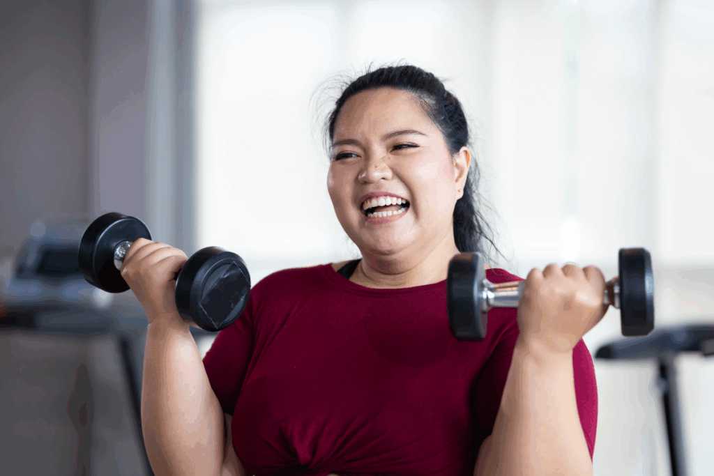 Mulher usando blusa vermelha e sorrindo enquanto levanta pesos de academia
