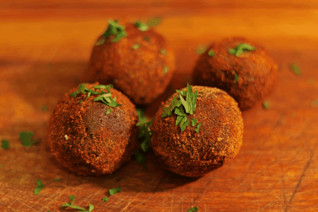 Quatro bolinhos de feijoada fritos e crocantes salpicados com salsinha picada sobre tábua de madeira.