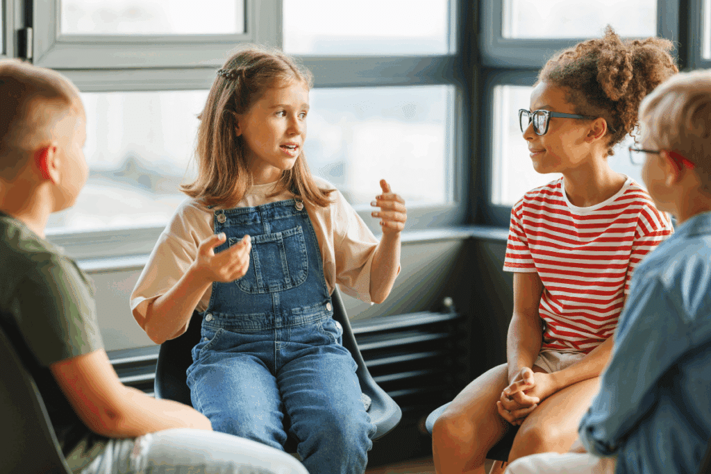 Menina sentada em um círculo com crianças, conversando e gesticulando com as mãos