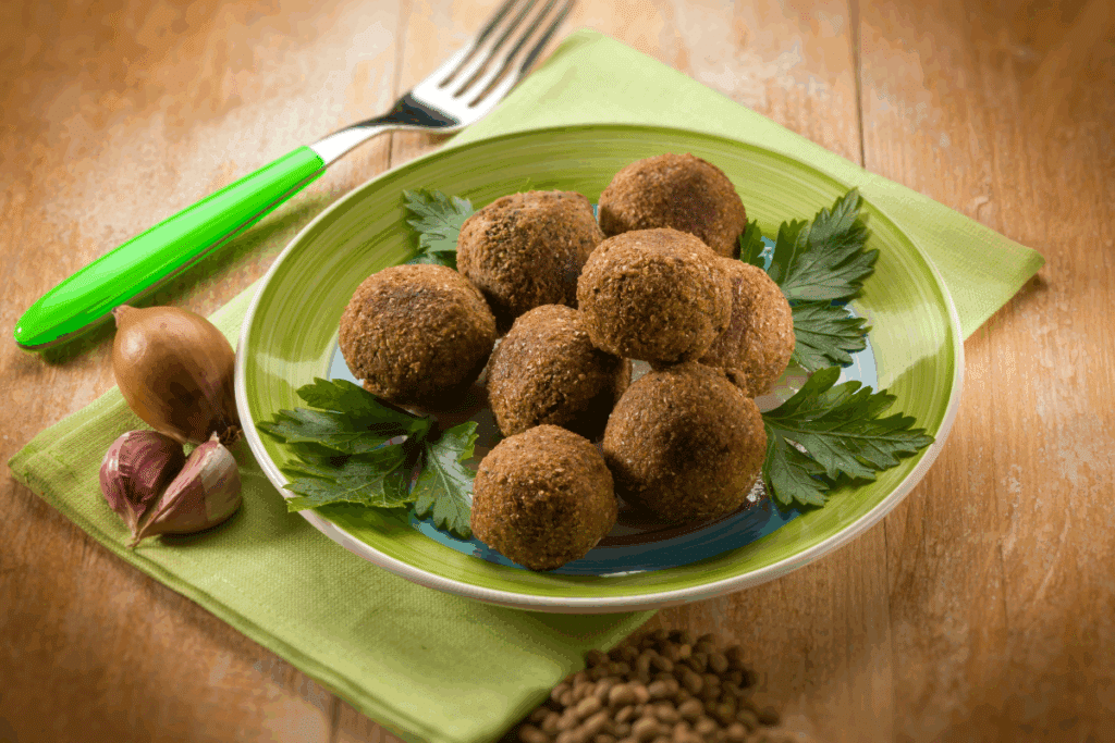 Falafel de lentilha servido em prato verde com folhas em cima de guardanapo verde em cima de mesa de madeira