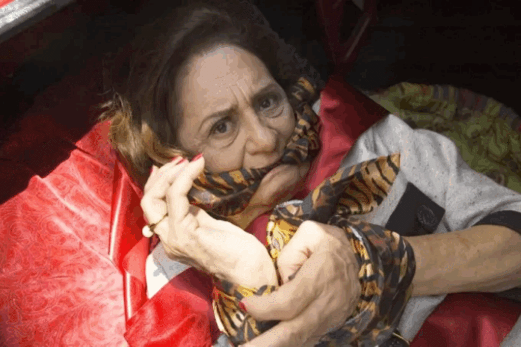 Mulher idosa com mãos e mordaça feitas de lenços estampados de animal print deitada em almofada vermelha