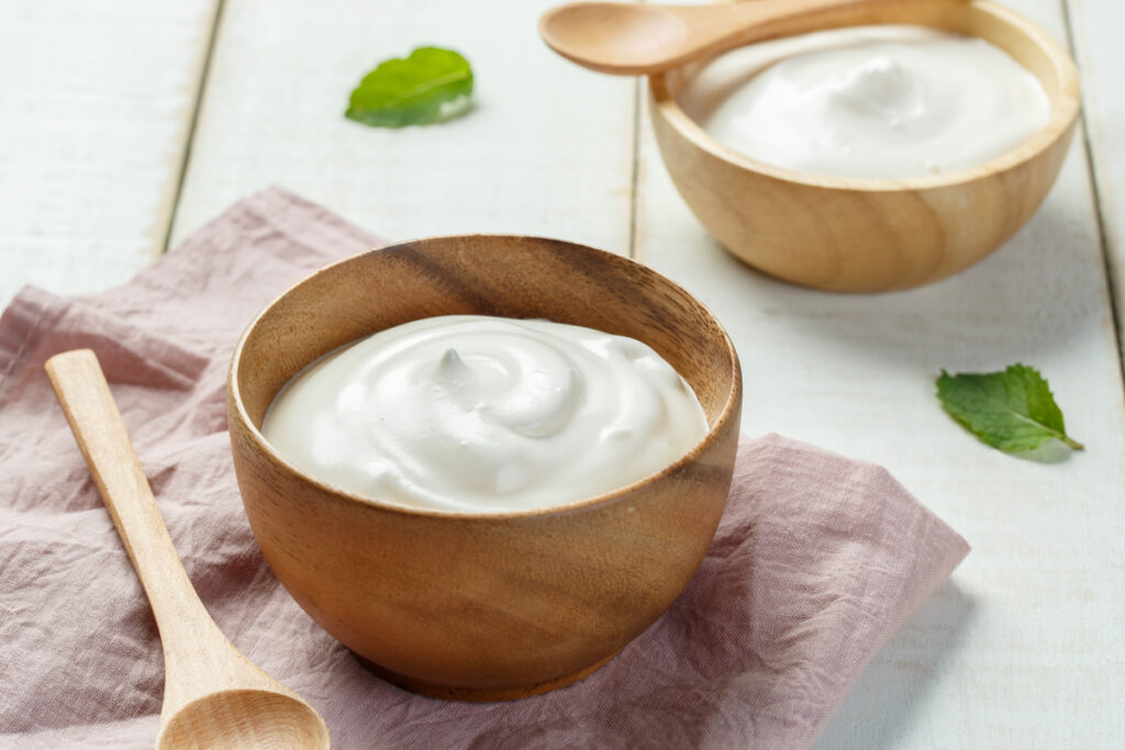 Recipiente de madeira com iogurte branco em cima de uma mesa com pano rosa-claro