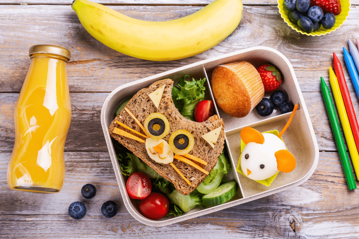 Lancheira infantil com sanduíche de gato, muffin, frutas, suco de laranja e ratinho feito de ovo cozido
