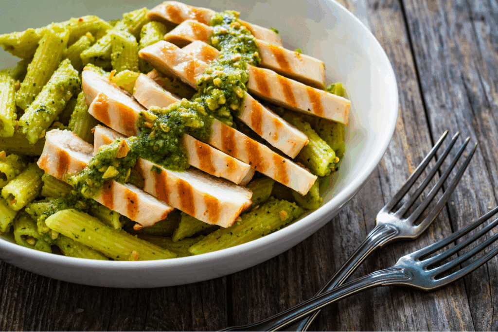 Macarrão proteico com pesto de amêndoas e frango grelhado em bowl branco sobre mesa de madeira