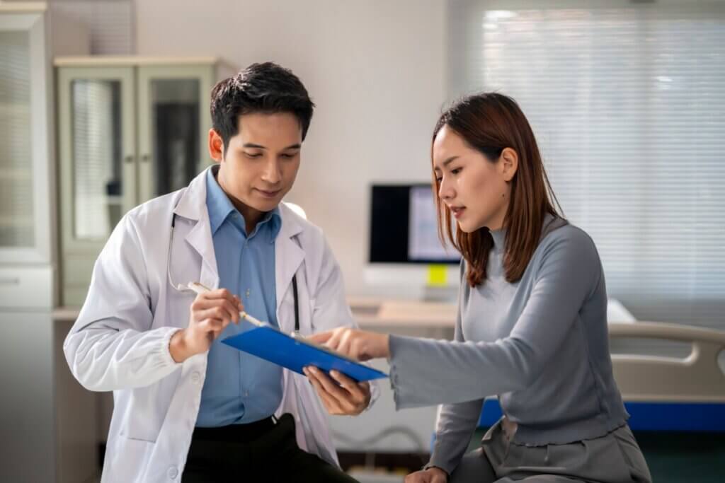 A imagem mostra uma consulta médica, com um profissional de saúde e uma paciente analisando informações em uma prancheta. A cena transmite um momento de orientação e esclarecimento, no qual médico e paciente discutem resultados, sintomas, diagnóstico ou opções de tratamento