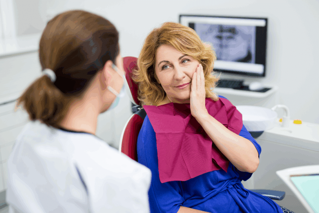 Mulher com cabelo curto, usando camisa azul e com mão na boca em avaliação com dentista