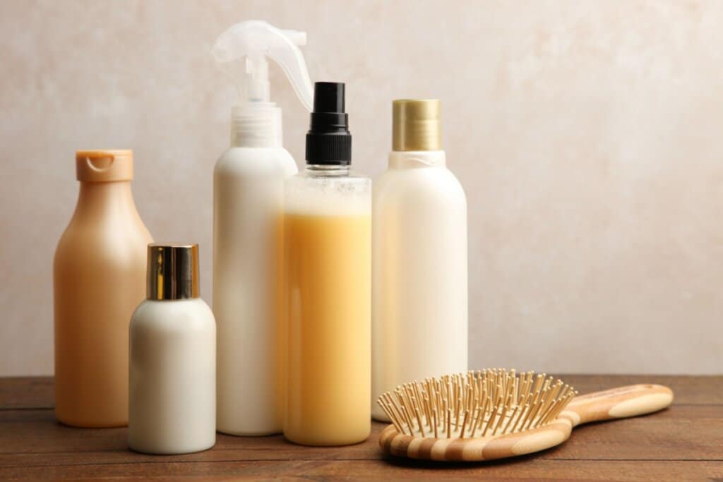 Vidros de produtos para cabelo em cima de mesa de madeira e ao lado uma escova de cabelo de madeira