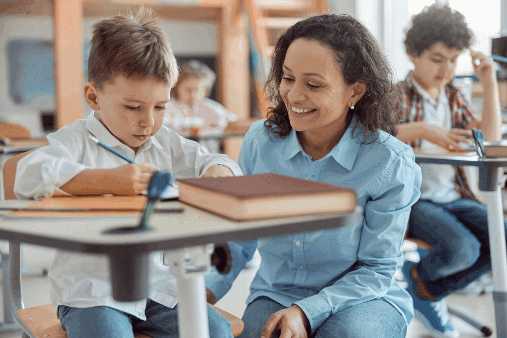 Professora auxiliando aluno enquanto ele faz tarefa na sala de aula