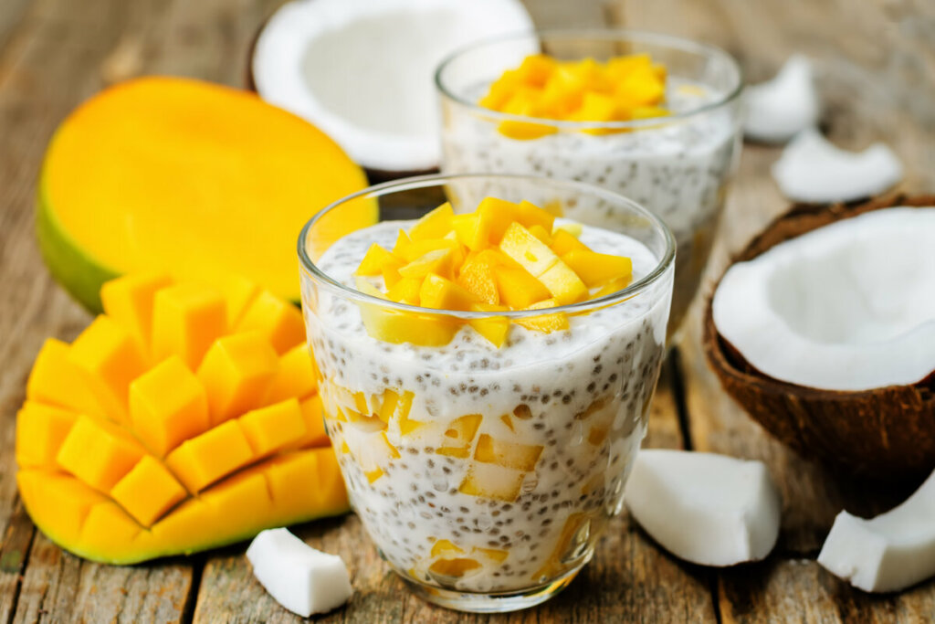 Copo de vidro com pudim de chia e pedaços de manga em cima de uma mesa de madeira