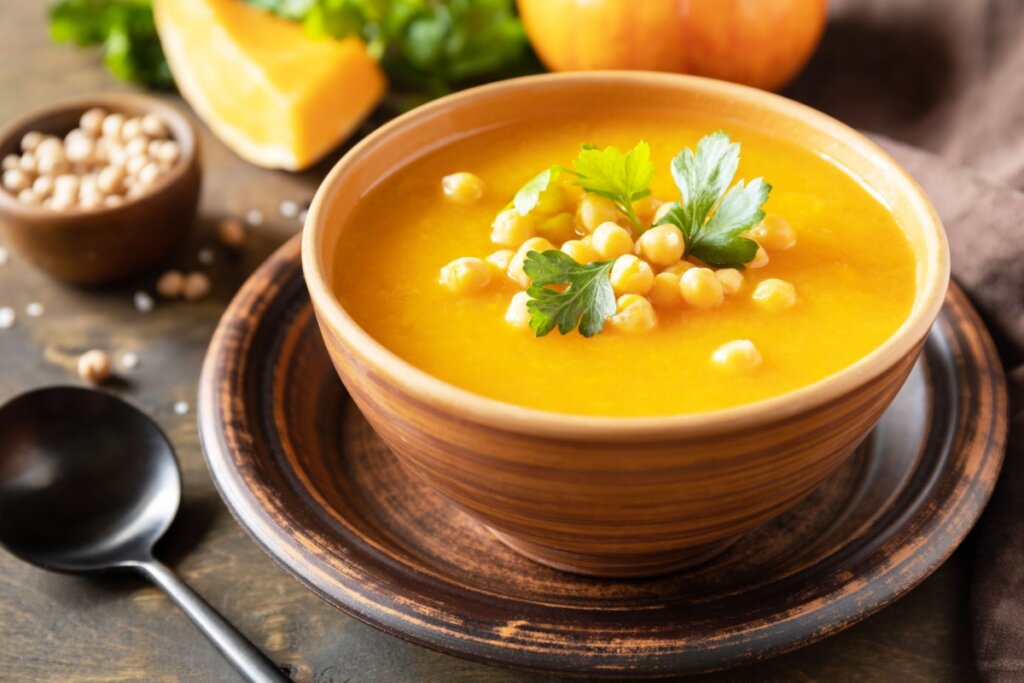 Sopa cremosa de abóbora servida em tigela de cerâmica, com grão-de-bico e salsinha fresca