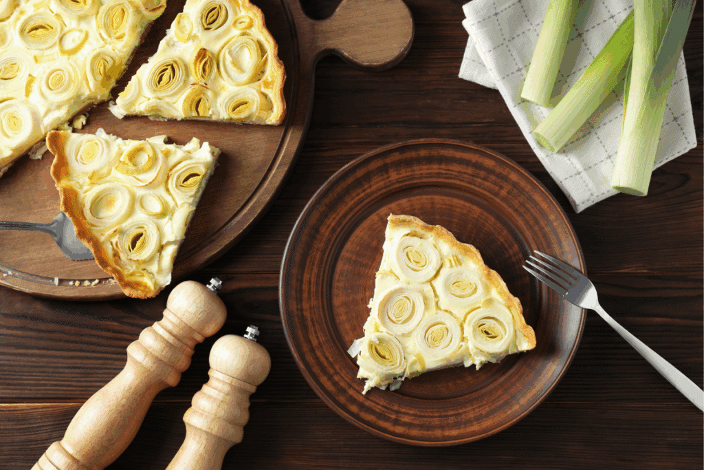 Pedaço de torta de alho-poró servido em prato marrom. Ao lado, outros dois pedaços sobre tábua de madeira 