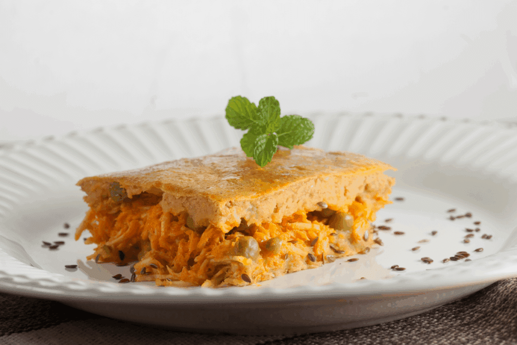Torta de frango com ervilha servido em prato branco em cima de mesa de madeira