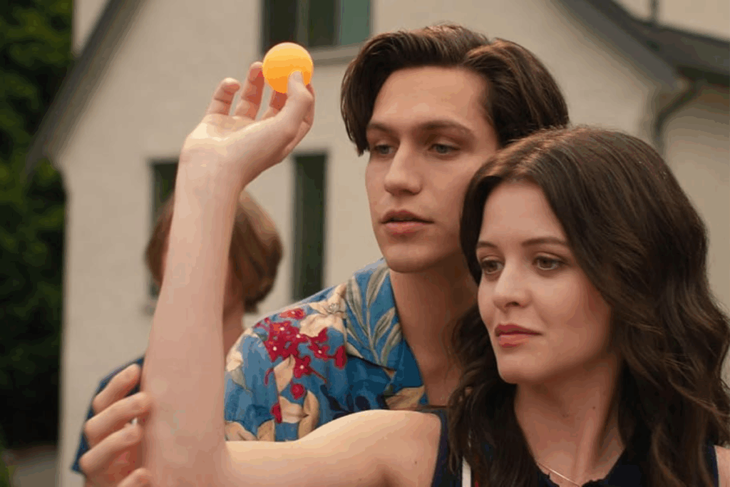 Imagem com um rapaz de camisa florida segurando uma bolinha laranja no ar enquanto orienta a posição do braço de uma jovem em "Como Perder Sua Popularidade"