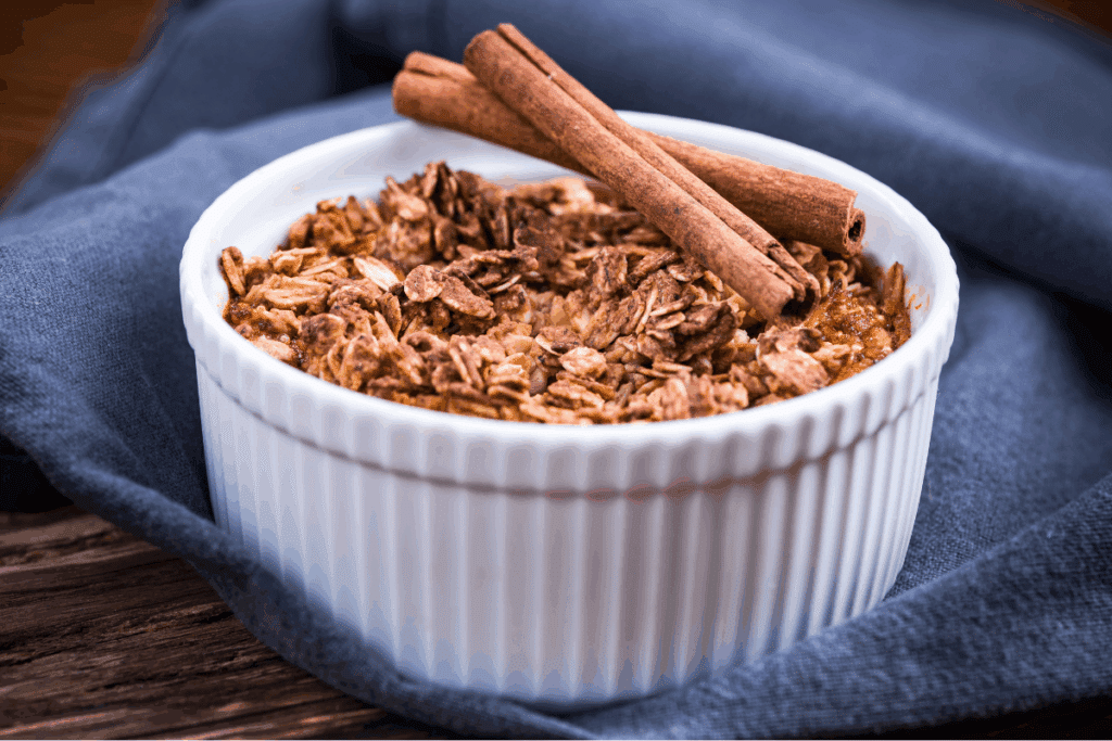 Crumble de maçã e aveia em ramequim cerâmico branco com duas canelas em pau cruzadas no topo