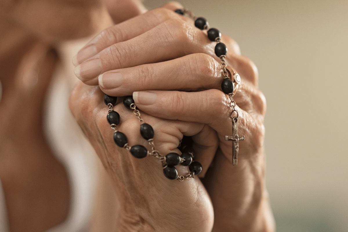 Mãos feminina juntas segurando um terço