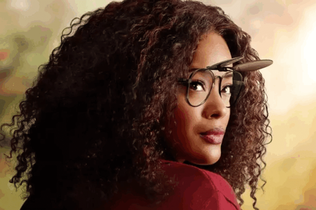 Retrato de uma mulher com cabelo cacheado volumoso, olhando para trás e usando óculos com lentes basculantes levantadas em "Um Mundo Diferente"