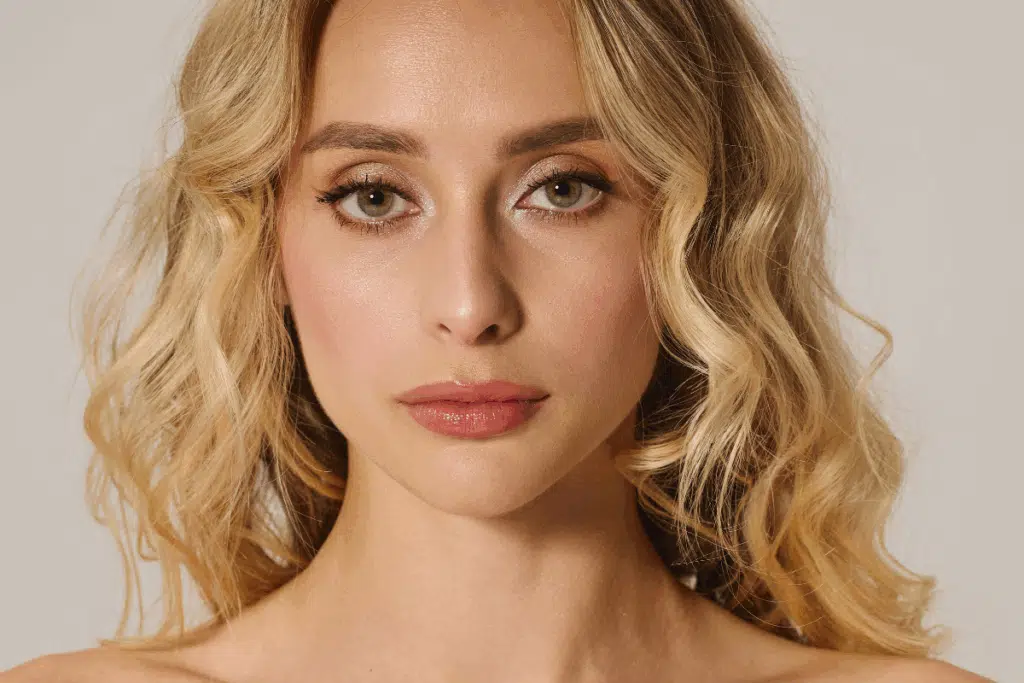Mulher com cabelo loiro-mel ondulado no estilo Y2K Honey, olhos claros e maquiagem em tons neutros.
