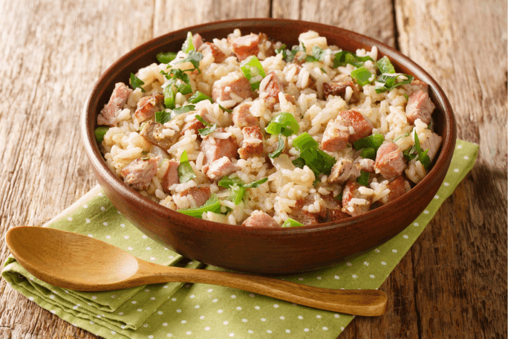 Recipiente marrom com arroz carreteiro em cima de uma mesa de madeira com pano verde e colher de madeira