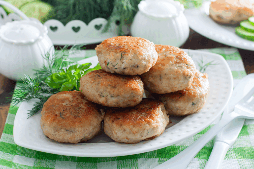 Bolinhos de pescada-branca assados, dourados e empilhados em prato branco, sobre toalha xadrez verde e branca.