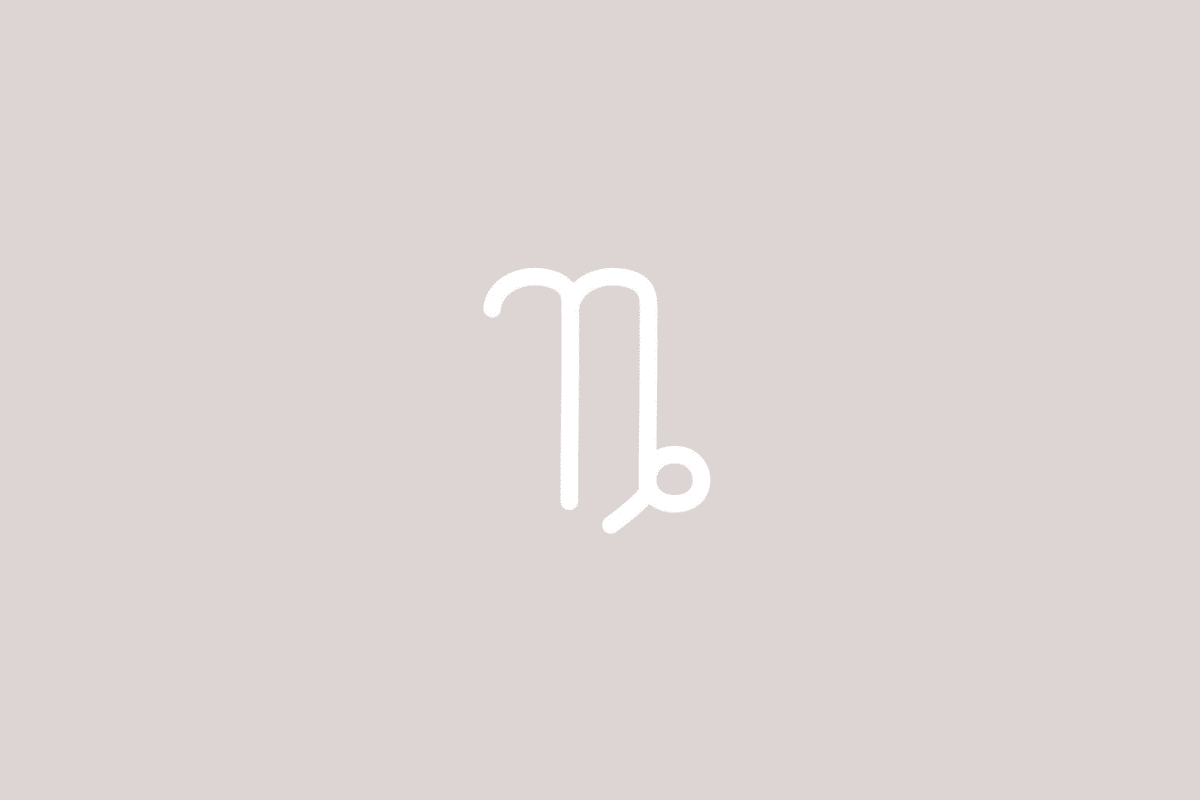 Imagem de fundo bege-acinzentado liso. No centro, o símbolo branco de Capricórnio é composto por duas linhas verticais com topo arredondado (semelhante à letra "n"), terminando à direita num laço circular com um pequeno traço oblíquo apontado para baixo