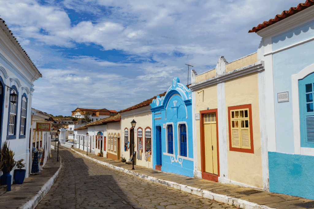 Rua de paralelepípedos do centro histórico da Cidade de Goiás (Goiás Velho), emoldurada por casarios coloniais de fachadas coloridas sob céu ensolarado