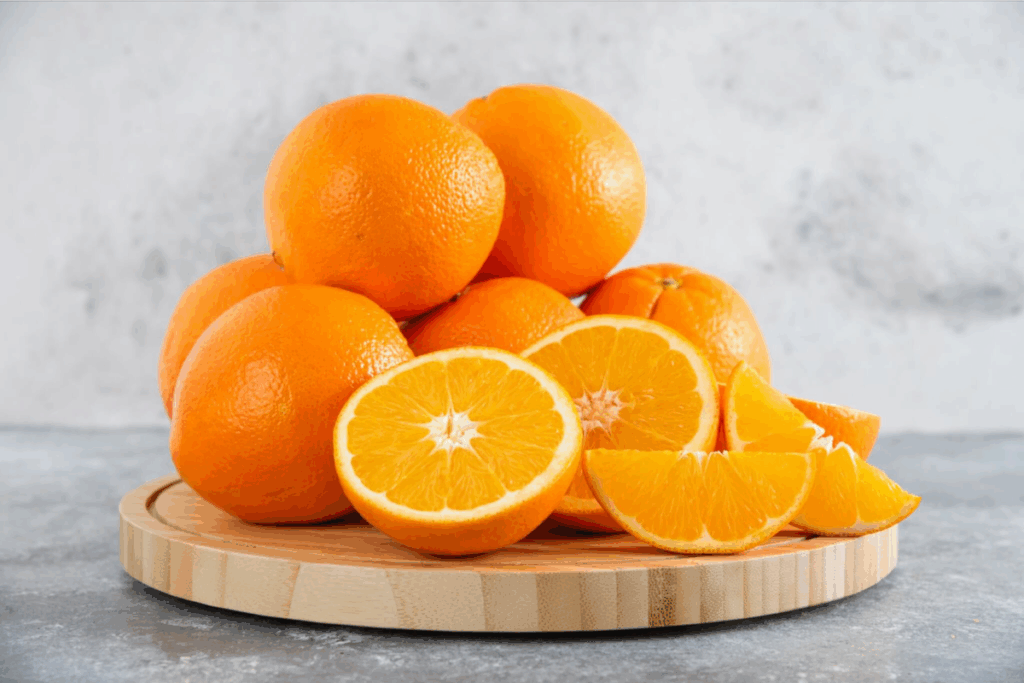Laranjas inteiras, cortadas ao meio e em fatias sobre uma tábua de madeira.