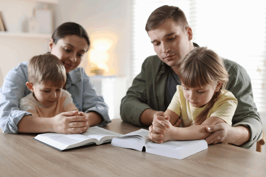 Pais e filhos reunidos à mesa com livros abertos durante momento de orações em família.