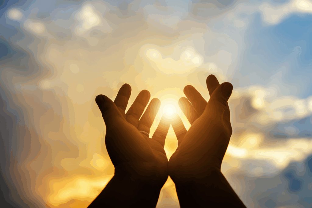Silhueta de mãos abertas voltadas para o céu ao pôr do sol, capturando a luz solar entre os dedos