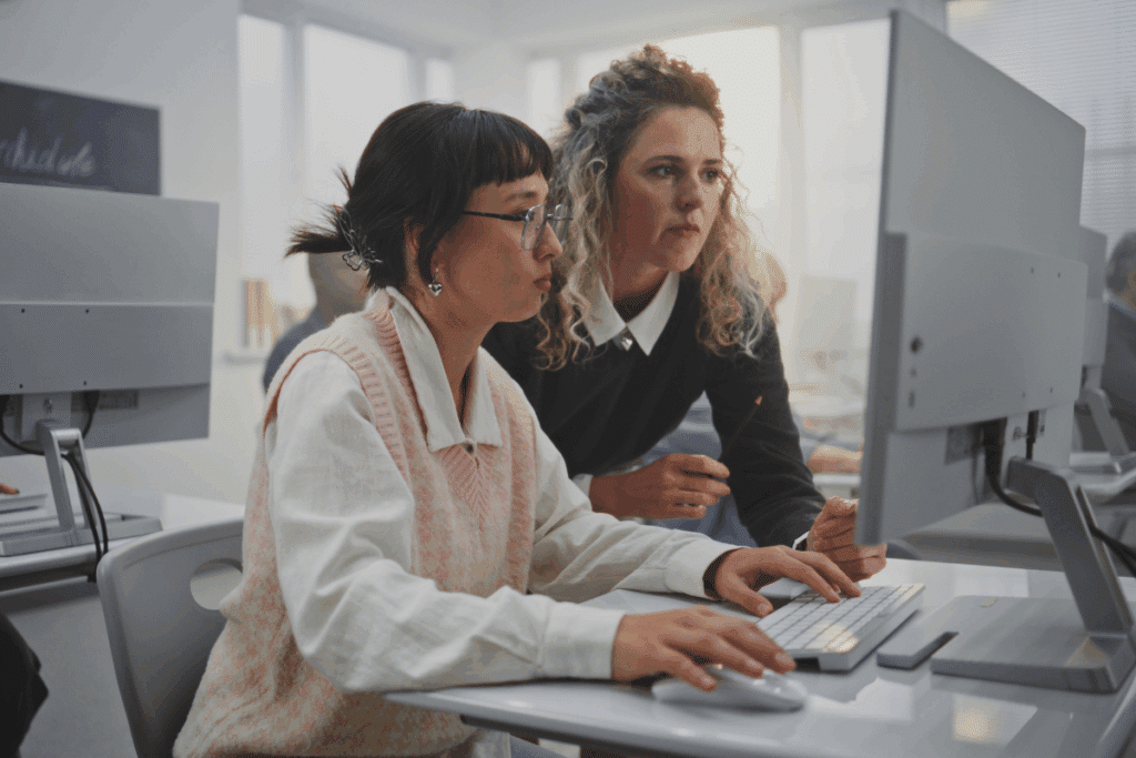 Duas mulheres em um escritório moderno observam concentradas a tela de um computador enquanto uma delas digita no teclado