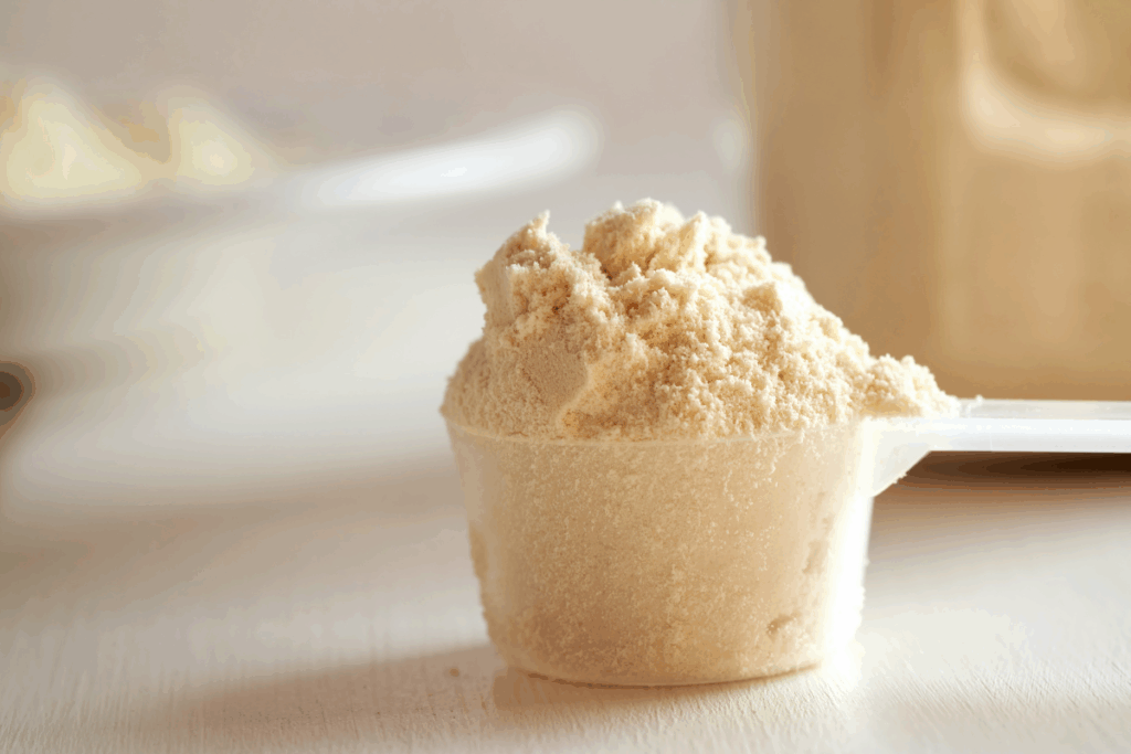 Um medador de plástico cheio de proteína em pó  na cor bege/creme, em foco sobre uma superfície clara