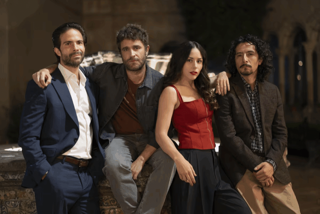 Quatro pessoas bem vestidas estão lado a lado ao ar livre, três homens e uma mulher, em pose amigável.