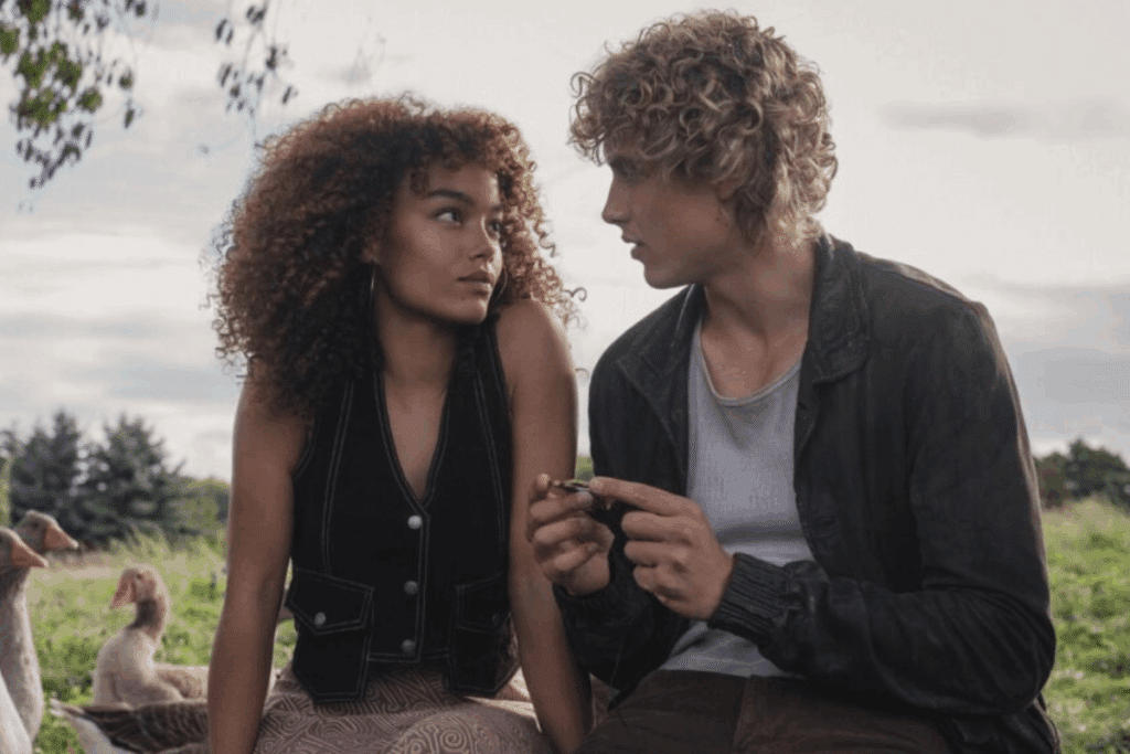 Um casal jovem está sentado ao ar livre perto de gansos, olhando um para o outro enquanto seguram um pequeno objeto nas mãos