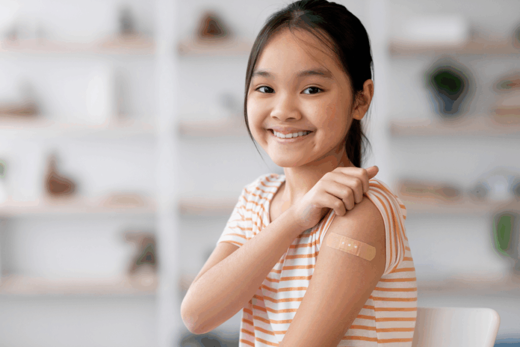 Menina sorridente de camiseta listrada apontando para um curativo no braço após ser vacinada